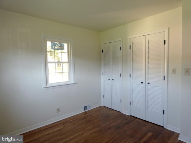 unfurnished bedroom featuring two closets and dark wood-type flooring