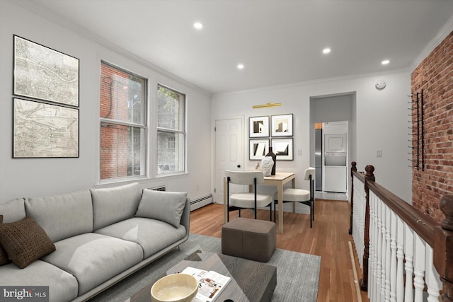 living room with ornamental molding, brick wall, baseboard heating, stacked washer / dryer, and light wood-type flooring