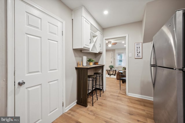 kitchen with light wood-type flooring, stainless steel refrigerator, white cabinetry, and ceiling fan