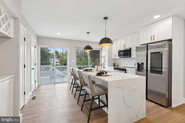 kitchen with light hardwood / wood-style floors, white cabinetry, a center island with sink, appliances with stainless steel finishes, and light stone countertops