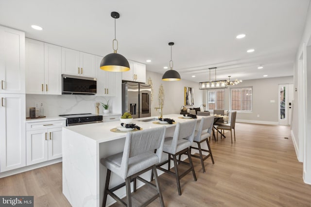 kitchen with hanging light fixtures, a center island with sink, white cabinetry, stainless steel appliances, and light hardwood / wood-style floors