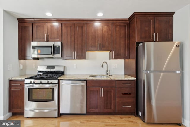 kitchen with appliances with stainless steel finishes, sink, light stone counters, and light hardwood / wood-style flooring