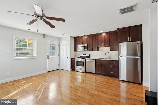 kitchen featuring stainless steel appliances, light hardwood / wood-style floors, sink, light stone countertops, and ceiling fan