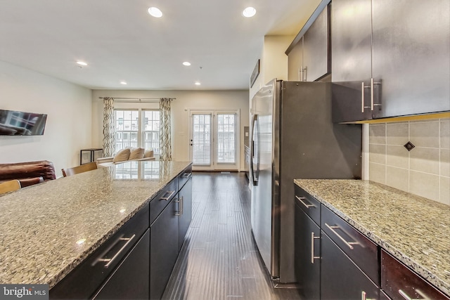 kitchen featuring light stone counters, tasteful backsplash, stainless steel refrigerator, a breakfast bar area, and dark hardwood / wood-style flooring