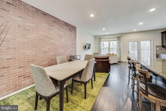 dining area featuring brick wall and dark wood-type flooring