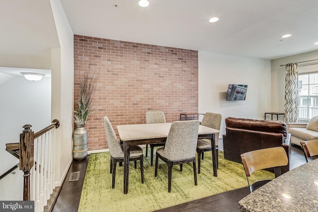 dining space with dark wood-type flooring and brick wall