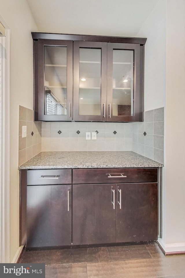 bar featuring light stone counters, dark brown cabinetry, and backsplash