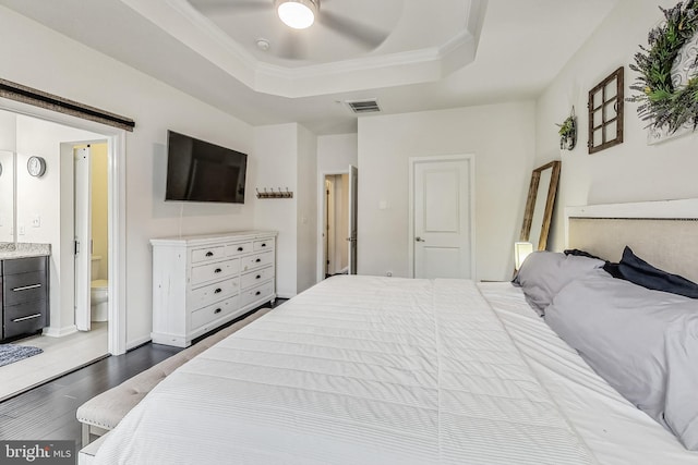 bedroom with ceiling fan, a tray ceiling, connected bathroom, and dark hardwood / wood-style floors