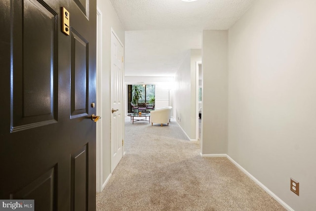 hallway with a textured ceiling and light colored carpet