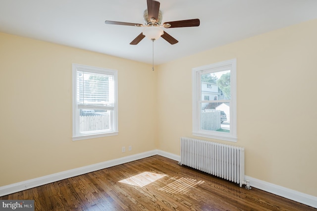 empty room with ceiling fan, dark hardwood / wood-style floors, radiator heating unit, and a wealth of natural light