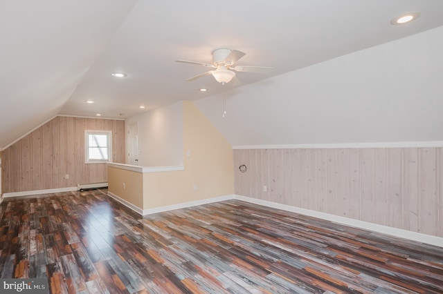 additional living space with ceiling fan, vaulted ceiling, wood walls, and dark hardwood / wood-style flooring