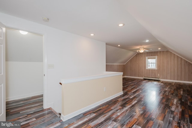 additional living space featuring vaulted ceiling, dark wood-type flooring, wood walls, baseboard heating, and ceiling fan