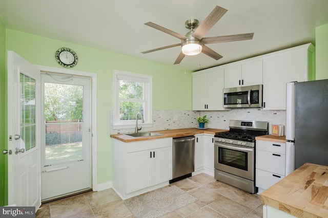 kitchen featuring appliances with stainless steel finishes, tasteful backsplash, white cabinets, butcher block counters, and sink