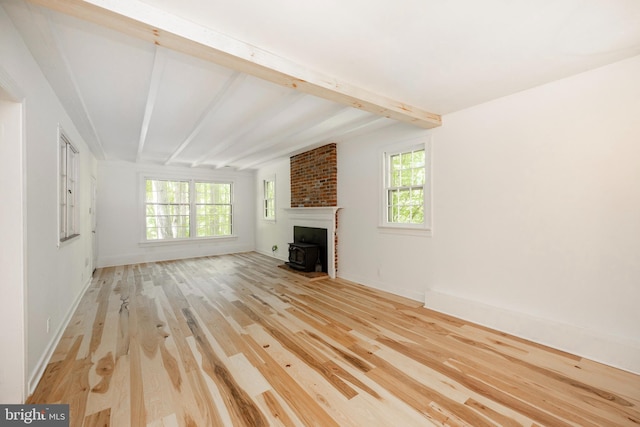 unfurnished living room with a wood stove, beamed ceiling, light wood-type flooring, and a healthy amount of sunlight