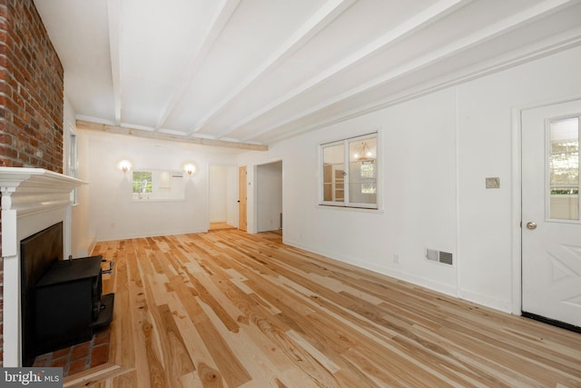 unfurnished living room with beamed ceiling, a wood stove, brick wall, a fireplace, and light wood-type flooring