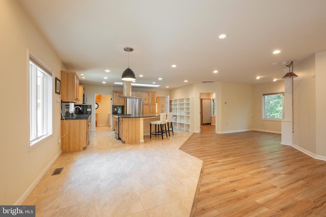 kitchen featuring hanging light fixtures, light hardwood / wood-style flooring, stainless steel refrigerator, a center island, and a breakfast bar area