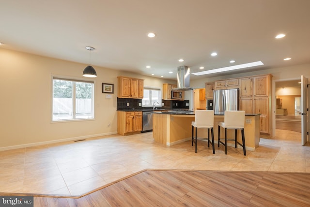 kitchen with island exhaust hood, stainless steel appliances, a center island, light wood-type flooring, and a kitchen bar