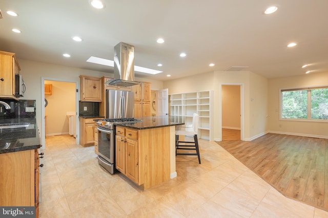 kitchen featuring dark stone counters, island range hood, a kitchen island, stainless steel appliances, and a skylight