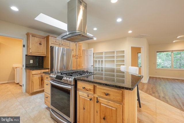 kitchen with appliances with stainless steel finishes, island range hood, light tile patterned floors, a center island, and dark stone counters