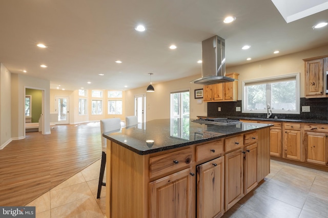 kitchen featuring a wealth of natural light, backsplash, island range hood, and a center island