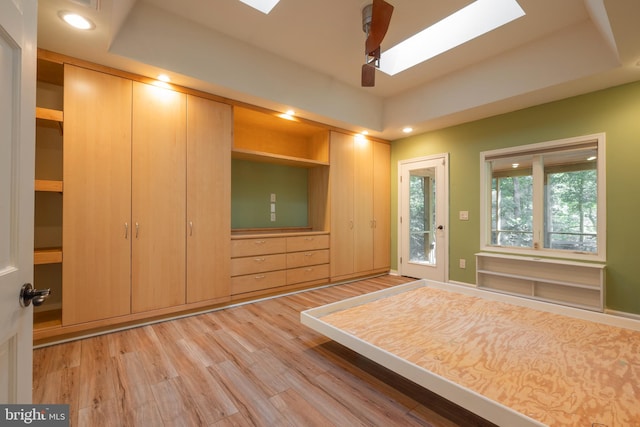 unfurnished bedroom featuring light hardwood / wood-style floors, a skylight, a raised ceiling, and ceiling fan