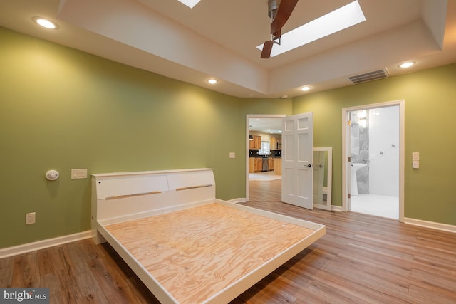 bedroom featuring wood-type flooring, connected bathroom, ceiling fan, and a skylight