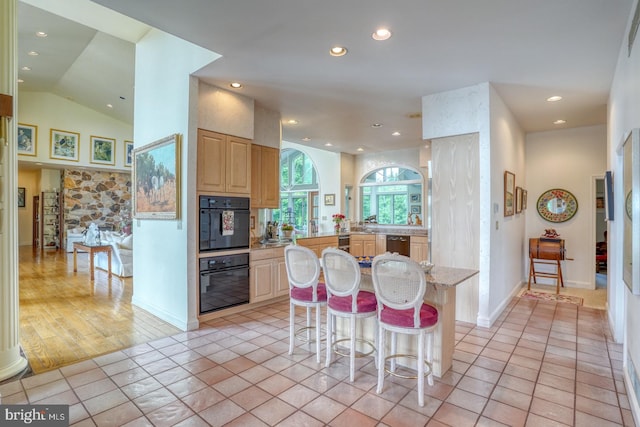 kitchen with light brown cabinets, light tile patterned floors, a kitchen island, dishwasher, and a kitchen breakfast bar