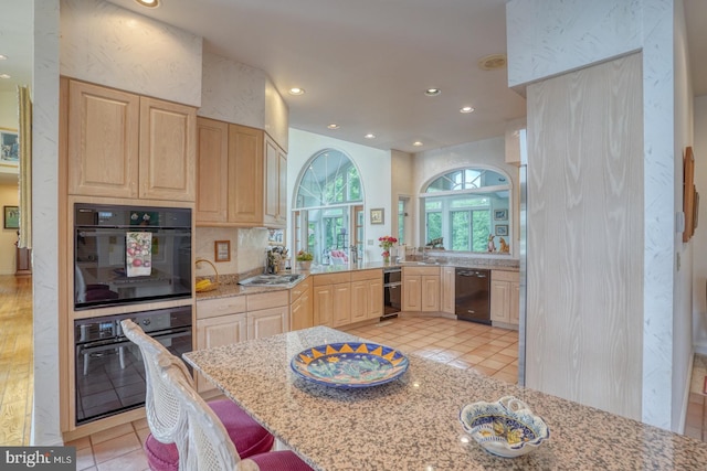 kitchen featuring light wood-type flooring, black appliances, light brown cabinetry, a breakfast bar area, and light stone countertops