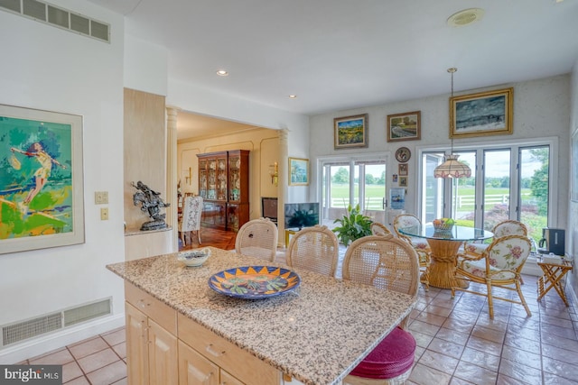 kitchen featuring pendant lighting, light brown cabinetry, decorative columns, light stone counters, and a center island