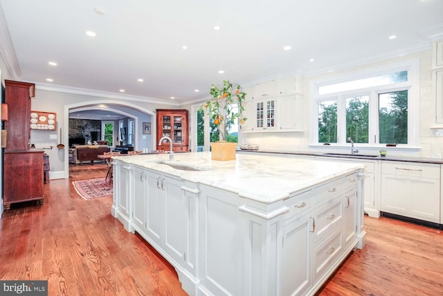 kitchen featuring white cabinetry, decorative backsplash, a kitchen island with sink, and light wood-type flooring