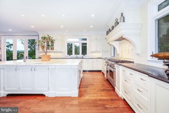 kitchen featuring range with two ovens, a kitchen island with sink, light wood-type flooring, and white cabinets