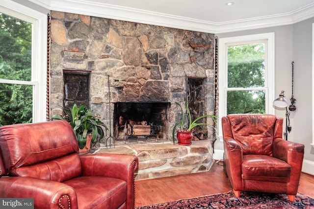 living room with crown molding, a stone fireplace, hardwood / wood-style flooring, and a healthy amount of sunlight