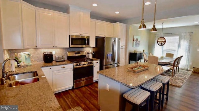 kitchen with appliances with stainless steel finishes, light stone counters, white cabinets, a center island, and sink