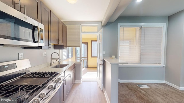 kitchen featuring appliances with stainless steel finishes, dark brown cabinets, beam ceiling, sink, and light hardwood / wood-style flooring