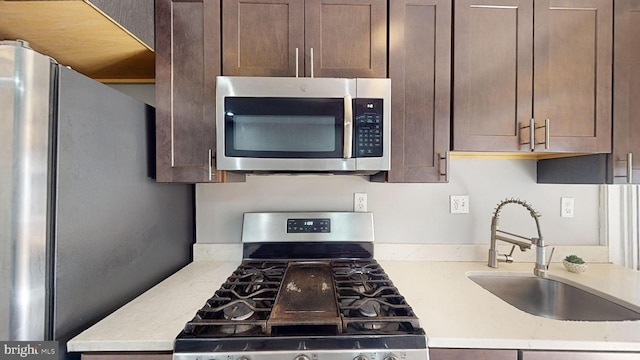 kitchen with dark brown cabinets, stainless steel appliances, sink, and light stone countertops