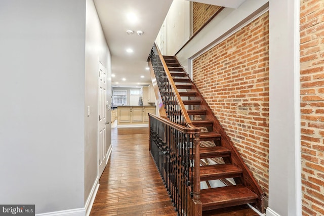 stairs with hardwood / wood-style floors and brick wall