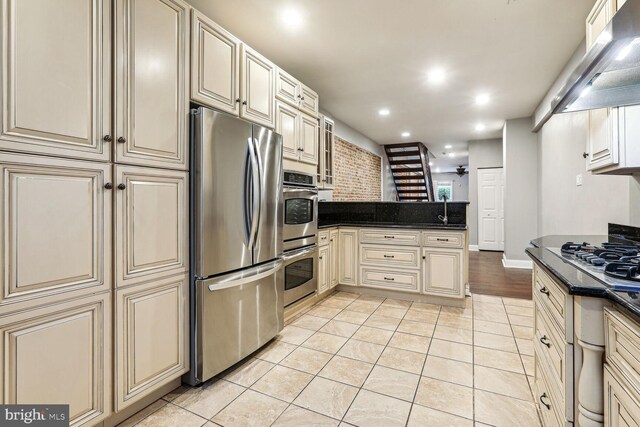 kitchen with cream cabinets, appliances with stainless steel finishes, light tile patterned floors, and ventilation hood