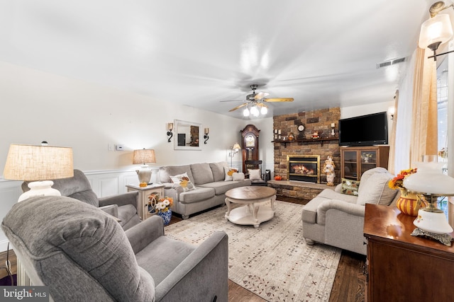 living room with wood-type flooring, a stone fireplace, and ceiling fan