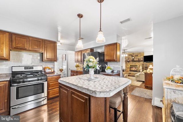 kitchen featuring dark wood-type flooring, a stone fireplace, black refrigerator, stainless steel range with gas cooktop, and a center island