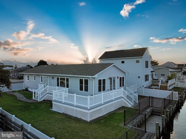 back house at dusk featuring a lawn and a deck with water view