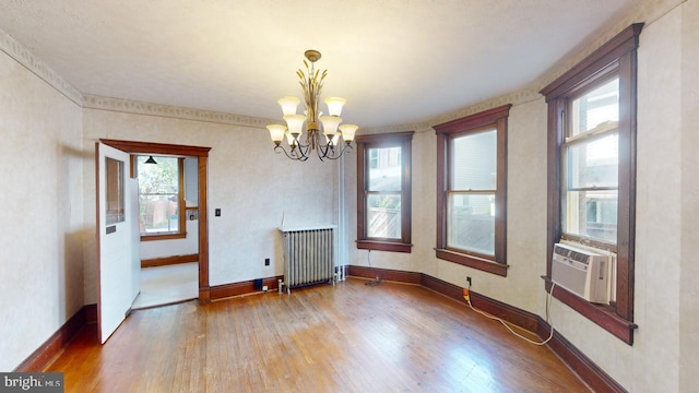 unfurnished dining area featuring a healthy amount of sunlight, wood-type flooring, radiator heating unit, and a chandelier