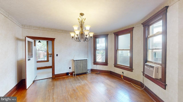 unfurnished dining area with a notable chandelier, cooling unit, radiator heating unit, baseboards, and wood finished floors