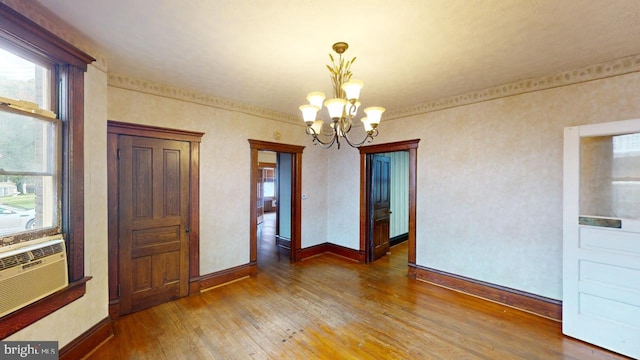 unfurnished dining area featuring an inviting chandelier, baseboards, wood finished floors, and cooling unit