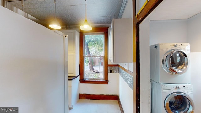 clothes washing area with stacked washing maching and dryer and ornamental molding