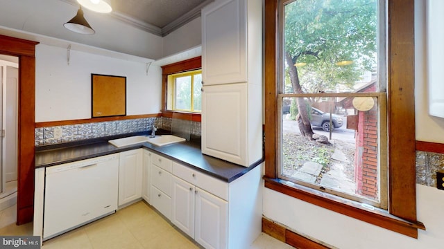 kitchen with crown molding, white dishwasher, dark countertops, white cabinets, and a sink