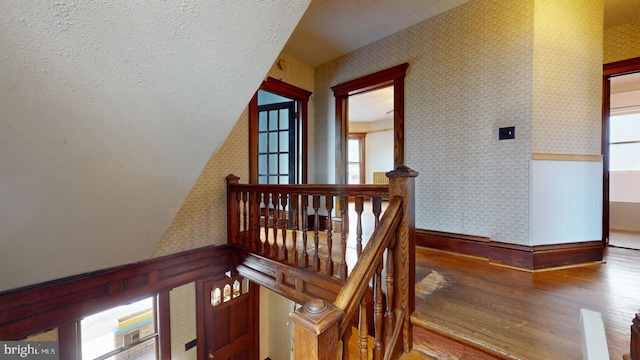 stairs with wood finished floors, a healthy amount of sunlight, baseboards, wallpapered walls, and vaulted ceiling