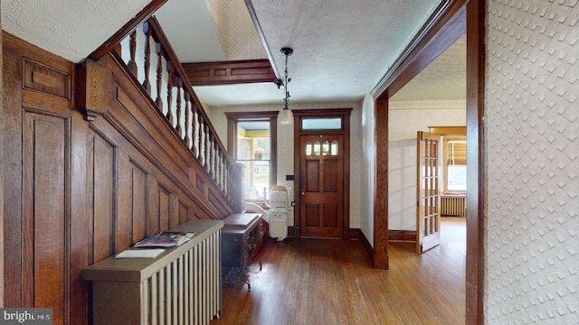 foyer with crown molding, wood-type flooring, a textured ceiling, and wooden walls