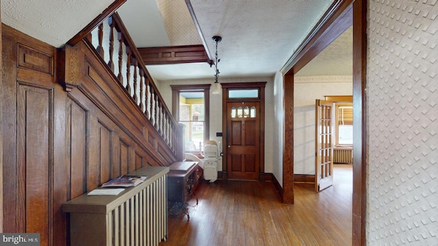entrance foyer with wood-type flooring, a textured ceiling, radiator, baseboards, and stairway