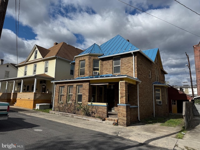 view of front of property featuring a standing seam roof, cooling unit, metal roof, and brick siding