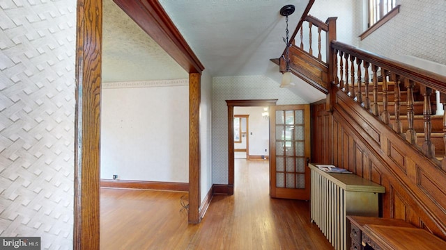 stairway with french doors, baseboards, wallpapered walls, wood finished floors, and vaulted ceiling